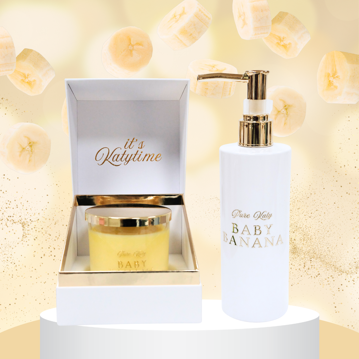 Elegantes Set mit einer Duftkerze und einer weißen Spenderflasche, beide mit goldener Schrift "Baby Banana" verziert. Die Kerze ist in einer luxuriösen Box mit der Aufschrift "It's Katytime" präsentiert. Im Hintergrund sind frische Bananenscheiben und ein goldener Schimmer zu sehen. Perfekt für ein hochwertiges und fruchtiges Dufterlebnis.
